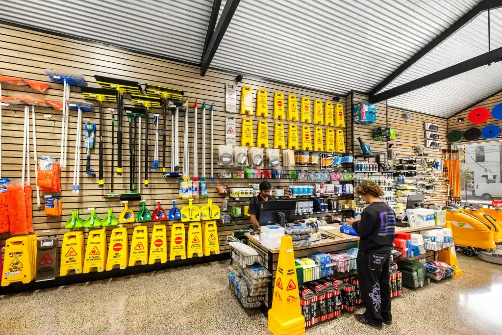 Customer browsing professional cleaning equipment in a trade showroom featuring walnut slatwall displays, retail shelving, and a customer service counter.