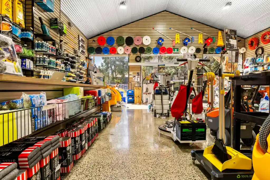 Wide aisle of a professional cleaning equipment showroom featuring retail shelving, floor cleaning machines, cleaning supplies, and organised display fixtures.